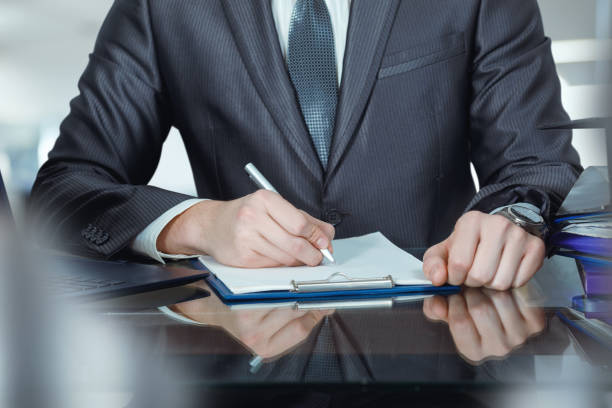 A business man signs a document at his desk in his office.