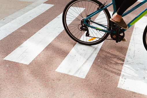 Close-up view of a woman's feet as she rides a bicycle across a pedestrian crossing.