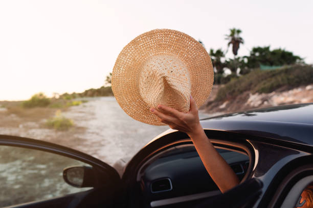 istock Hand holding a straw hat through a car window at sunset 2105037870