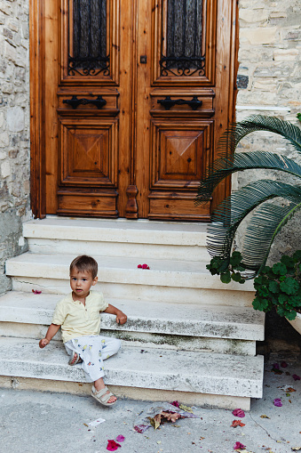 Toddler on steps of a rustic Mediterranean home entrance.
