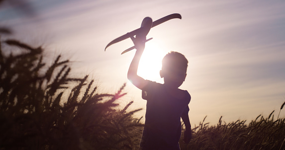 Silhouette, sunset and kid with airplane for flight, adventure and childhood development on field. Sky, wheat and boy with miniature toy in nature for freedom, holiday and playing at countryside