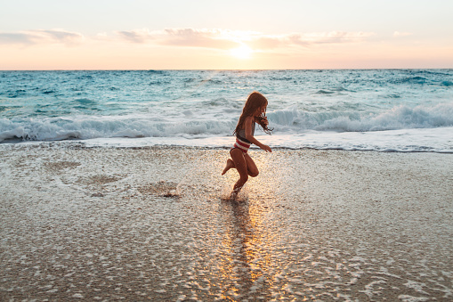 Brave girl enjoying the waves on the beach and splashing and playing on her summer vacation on the beautiful Greek Lefkada island