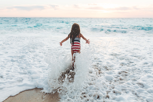 Brave girl enjoying the waves on the beach and splashing and playing on her summer vacation on the beautiful Greek Lefkada island