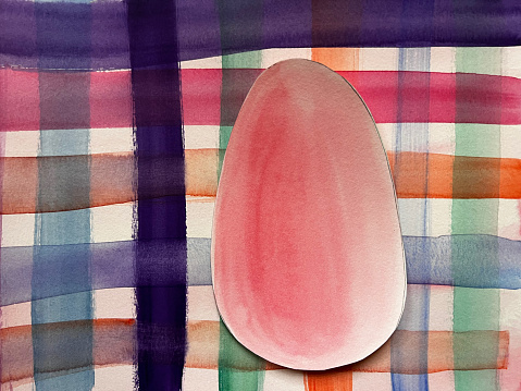An Easter egg decorated and painted by male hands is photographed over a light gray table with natural light