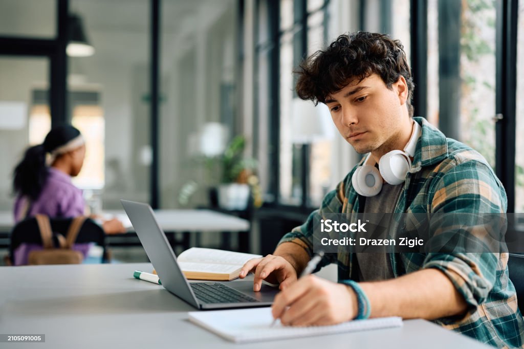 大学でノートパソコンでノートを取りながらノートを取る若い学生。 - 大学生のロイヤリティフリーストックフォト 大学でノートパソコンでノートを取りながらノートを取る若い学生。 - 大学生のロイヤリティフリーストックフォト