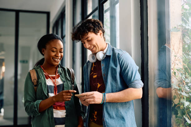 istock Happy college friends using cell phone in a hallway. 2105096294
