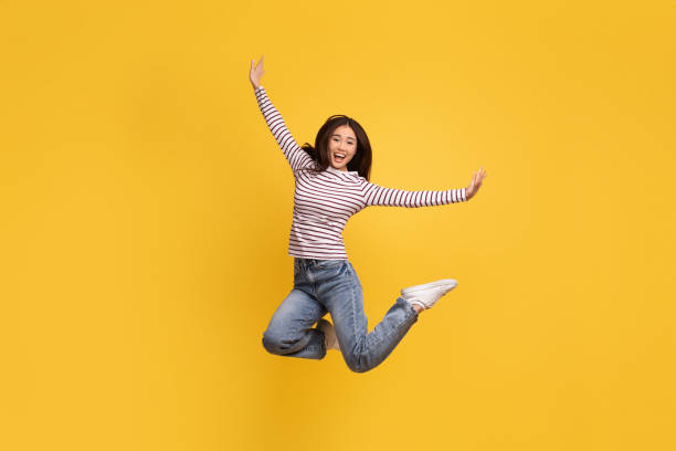 istock Overjoyed young chinese lady 20s jumping on yellow background 2105099031
