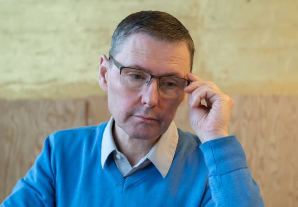 Close up of a man wearing glasses looking tired or in pain, one person, indoors.