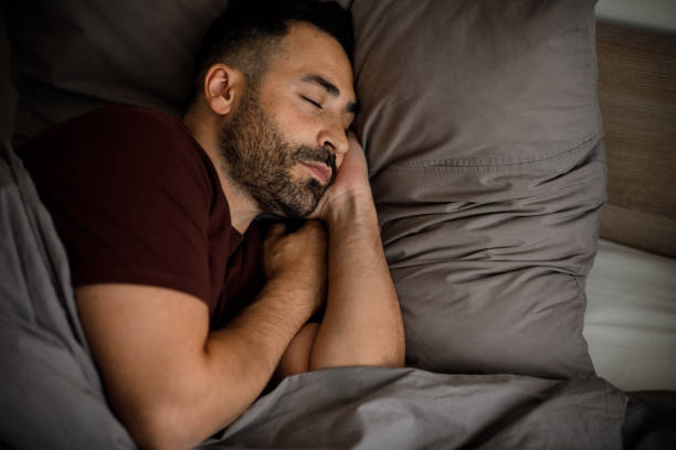 istock A calm young man with a beard sleeps in bed, on a soft pillow under a blanket in a bedroom interior. 2105147077