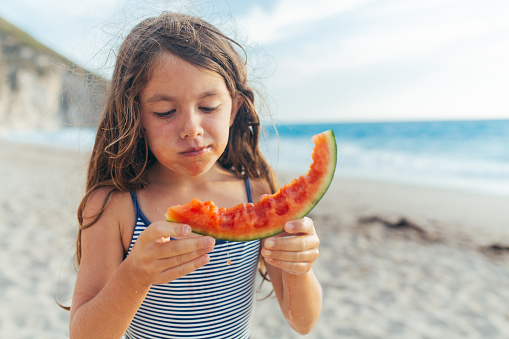 Girl eating juicy slice of watermelon on her summer beach vacation