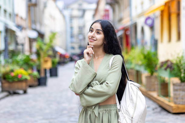 joven india hermosa mujer de pie afuera en una calle de la ciudad, posando con una mano en la cara y mirando hacia un lado sonriendo -   brunette  fotografías e imágenes de stock