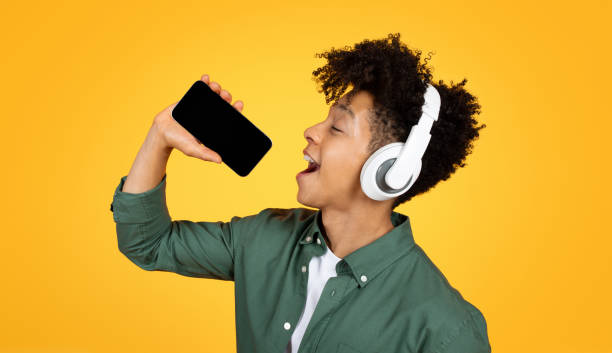 istock Joyful young black guy singing karaoke on yellow background 2105198291
