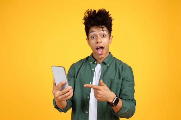 istock Emotional black guy pointing at phone in his hands 2105198803