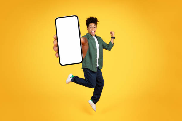 istock Joyful young black guy jumping with phone in his hand 2105198856
