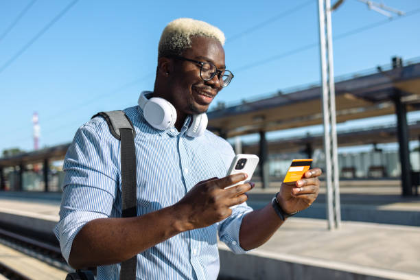 istock Young African American man using smart phone and credit card on a train station 2105290645