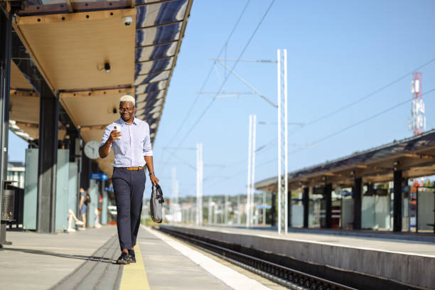 African American young man carrying a laptop bag and waiting a train on a railroad station