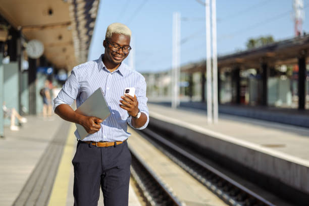 istock Young African American man carrying laptop and using smart phone on the train station 2105296467