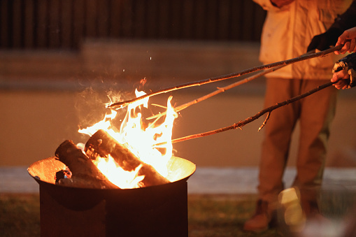 People engage in a traditional fire ritual, stoking the flames with long sticks against the backdrop of the night, creating a sense of warmth and ancestral connection.