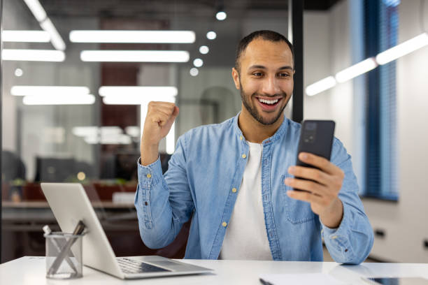 istock Excited businessman celebrating success with smartphone at office 2105421320