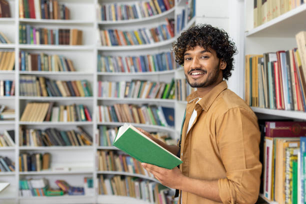 istock Man holding a book in a library full of shelves 2105437874