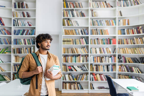 istock Young man with books standing in modern library 2105466206