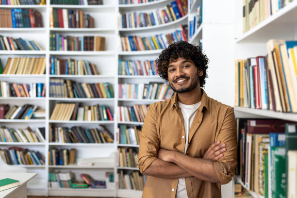 istock Confident young man smiling in a library with arms crossed 2105476264