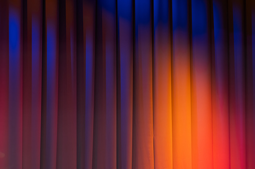 Closed theatrical curtain with colorful spot lights of stage illumination, background photo texture