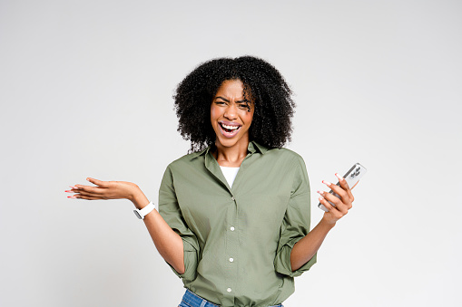 An African-American woman displays a perplexed expression while holding a smartphone, suggesting a moment of confusion or unexpected news received through her device