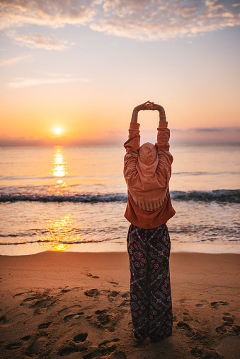 Young woman doing yoga and streching at sunrise by the sea.