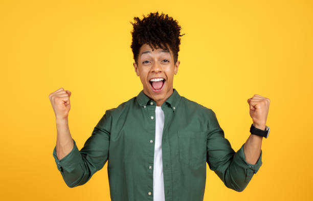 istock Thrilled young african american guy clenching fists on yellow 2105491449