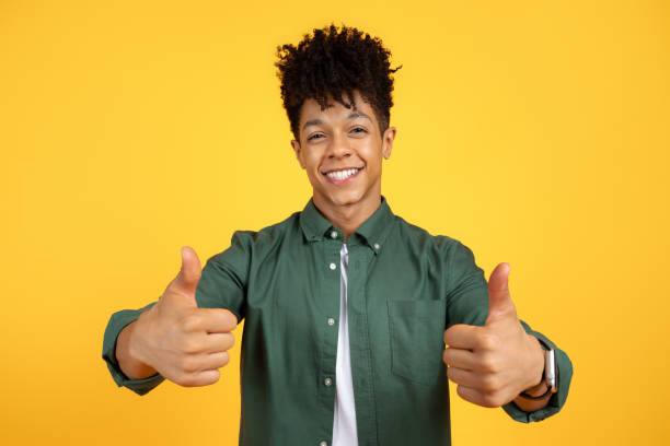 istock Positive young black guy gesturing thumbs up on yellow background 2105491453
