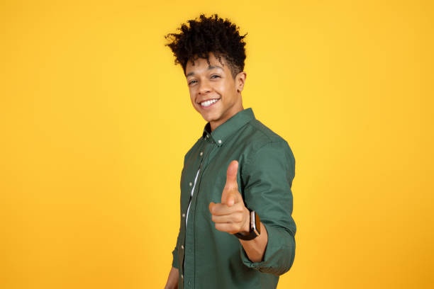 istock Stylish cool black guy pointing at camera, yellow background 2105491465