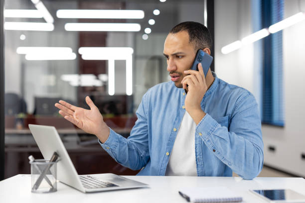 istock A man is talking on his cell phone while sitting at a desk 2105494840