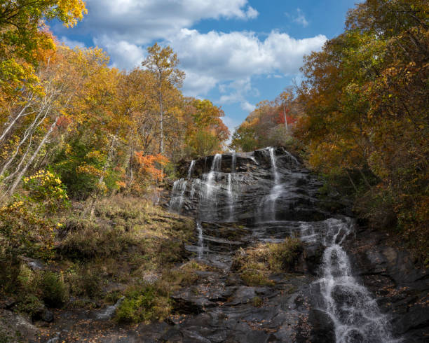 The top of Amicalola Falls makes a steep descent over a rocky cliff as viewed from the observation platform of the middle falls, surrounded by fall foliage with a blue sky.