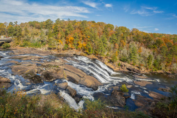 In a backdrop of fall foliage and blue sky, the scenic Towaliga River  cascades downstream over granite bedrock. Captured from Tranquility Trail in High Falls State Park in Georgia.