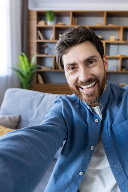 istock Cheerful man taking a selfie at home with a warm smile 2105536336