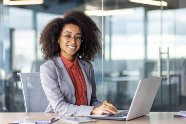 istock Attractive african american freelancer smiling at camera while keeping hands on portable computer keyboard. Successful interior designer enjoying productive busy day in modern shared coworking 2105537367