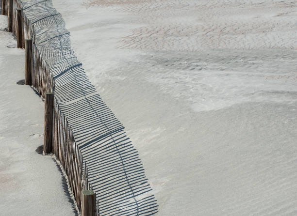 A closeup of a wooden fence in the dunes of the Atlantic coast in Anastacia State Park in Florida. Backlit by the morning sun the fence casts an interesting pattern of shadows and textures in sand.