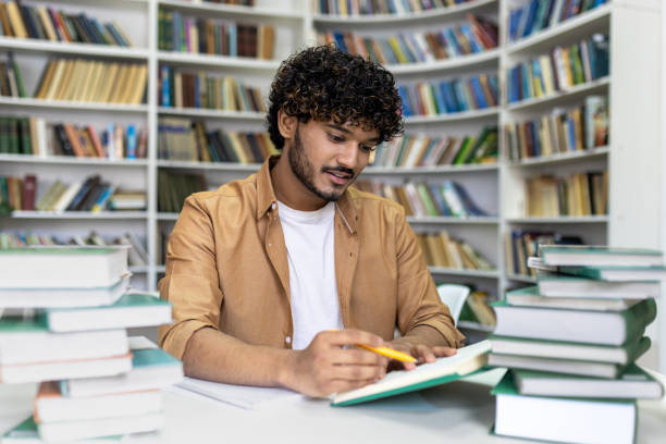 istock Focused student preparing for exams in the university library surrounded by books 2105585004