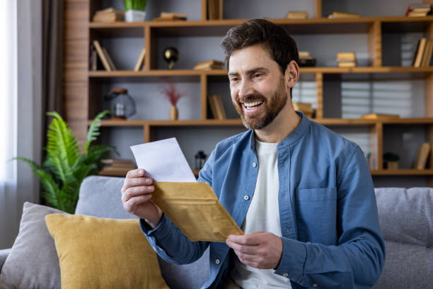 istock Smiling man reading a letter at home on the couch 2105614189