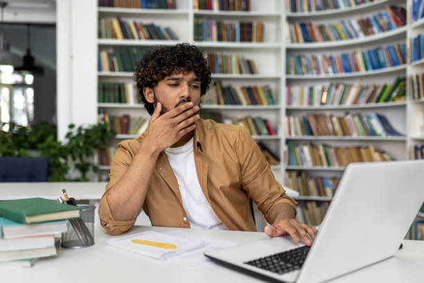 istock Pensive student studying with laptop in library, preparing for university exams 2105633553