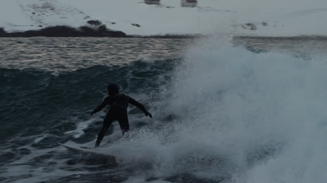Surfer quickly carves up and down picking up speed cutting back across arctic surfing wave, tracking follow