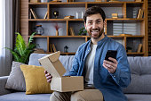 Man holding phone and package in cozy living room