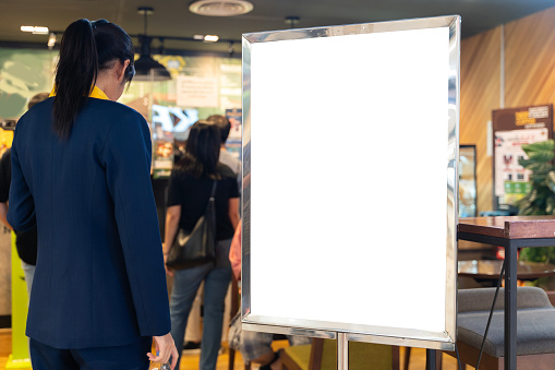 Shop sign on an easel mockup. White blank signboard stand near the entrance to the coffee shop, mock up, cafeteria blurred background can inserting the text of the customer. Clipping path.