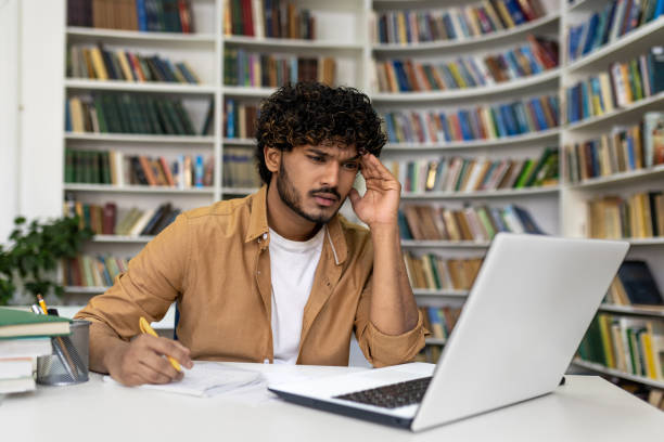 istock Concentrated male student studying with laptop in library 2105679193