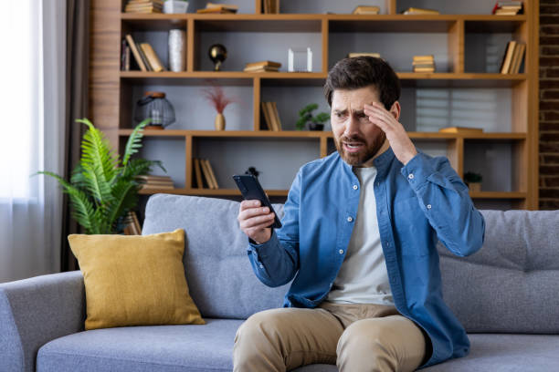 istock Worried man sitting on couch looking at smartphone 2105685851