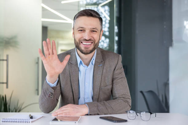 istock Friendly businessman waving hand in modern office setup welcoming partners 2105729337