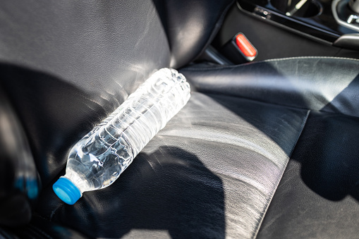 Plastic bottle of water placed on car seat and exposed to sun in sunny day,bottle of drinking water in car,sunlight,very hot,heating temperature,cause danger if parked in the sunshine for a long time