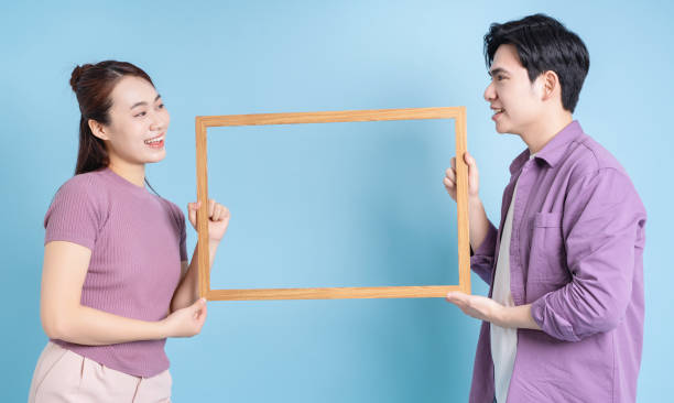 istock Young Asian couple holding photo frame on blue background 2105828835