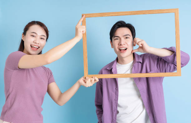 istock Young Asian couple holding photo frame on blue background 2105829167